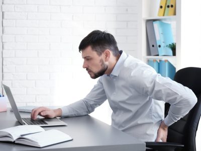 Posture concept. Man suffering from back pain while working with laptop at office