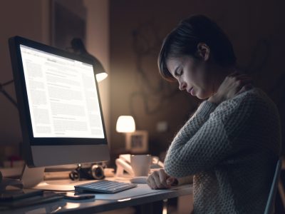 Young woman working with her computer late in the office and suffering from neck pain